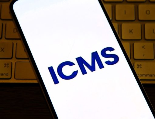 Smartphone exibindo sigla ICMS na tela, representando consulta à tabela ICMS e cálculo de impostos estaduais.
